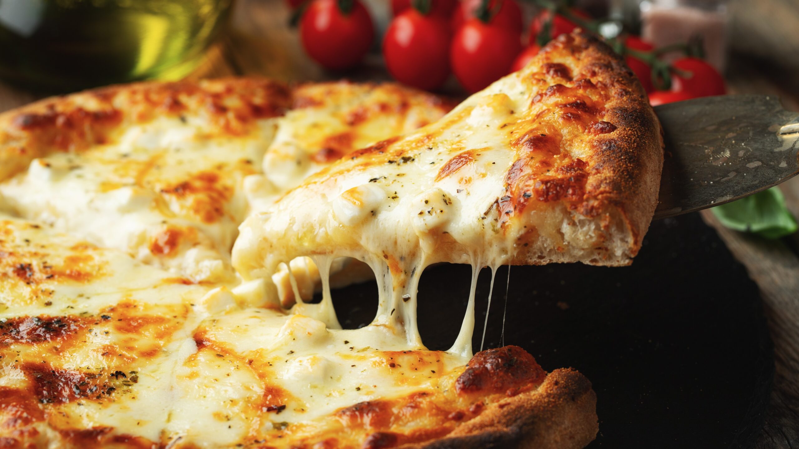 A slice of hot Italian pizza with stretching cheese. Pizza four cheeses with basil on a wooden background.